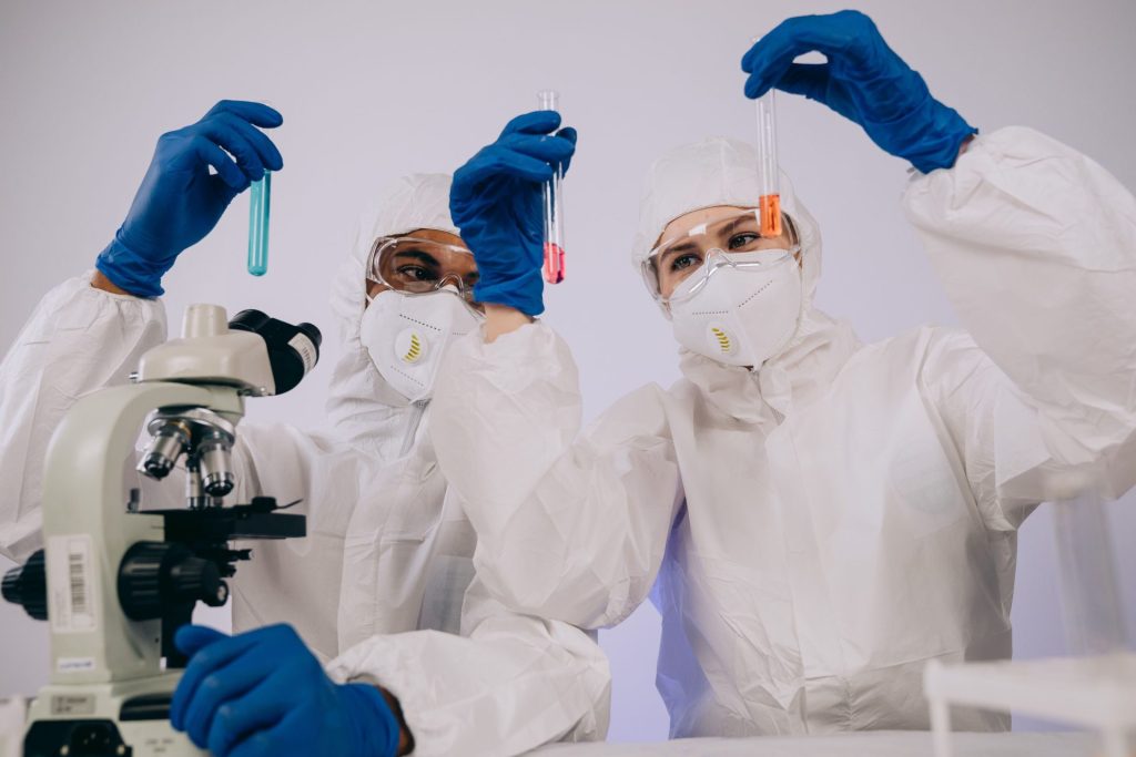 Two scientists in protective gear analyzing test tubes in a laboratory setting.